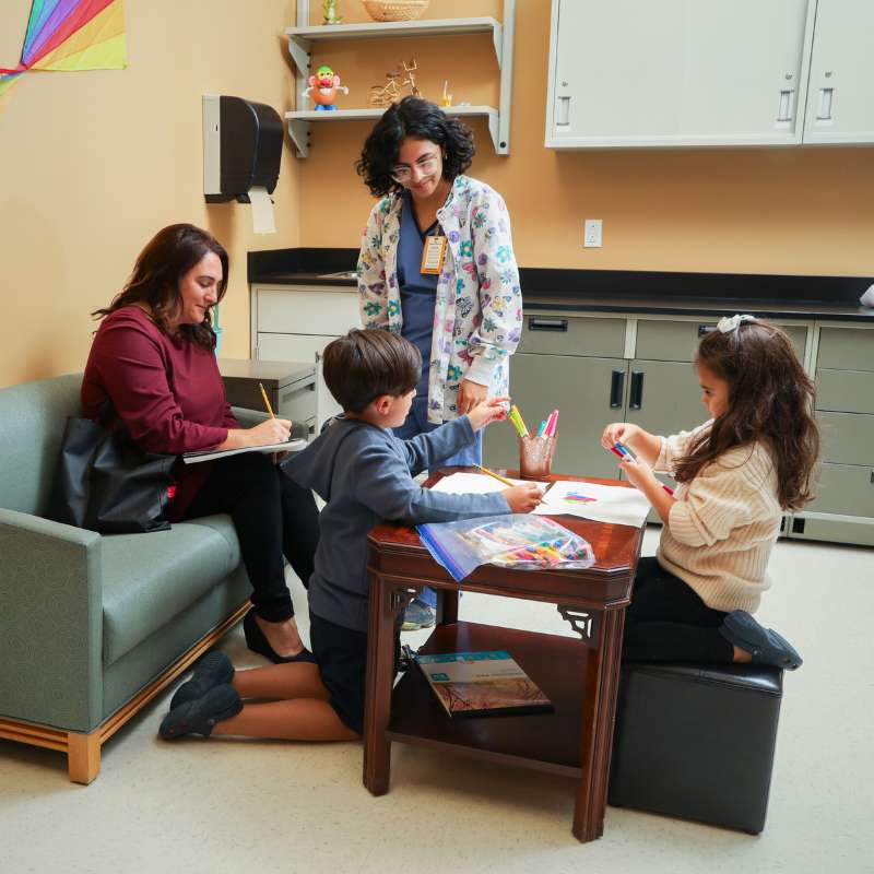 a mother completes paperwork while a clinical research nurse looks at her children