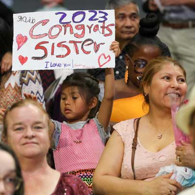 a child in the audience at the v.c.u. school of nursing graduation ceremony holding up a sign that reads 'congrats sister 2023'