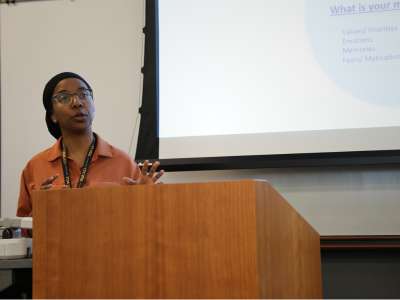 ana diallo, research faculty member, speaks from a podium in front of a projector screen