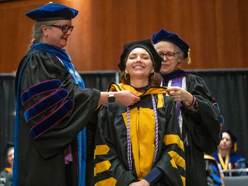 a graduating v.c.u. nursing student dressed in regalia receives adornments for her robe from faculty members