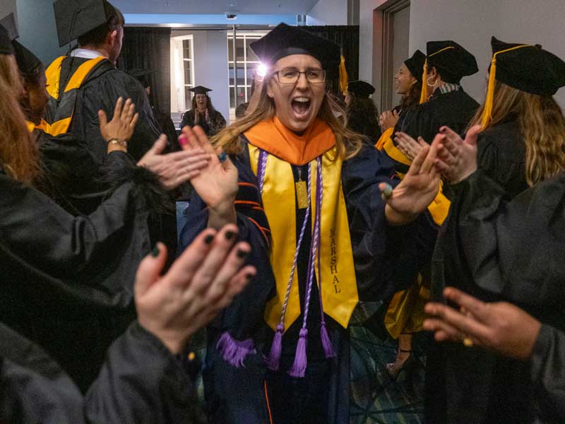 an excited v.c.u. school of nursing graduate gives high fives to other students at commencement