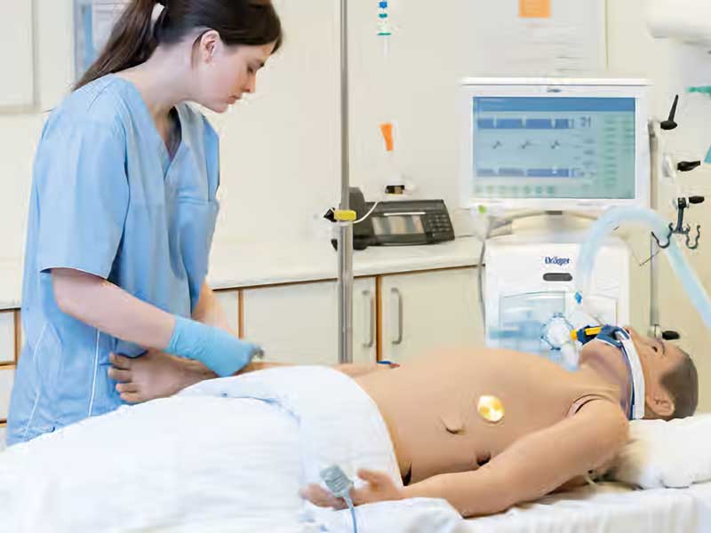 A nursing student performs chest compressions on an adult simulation mannequin in a hospital training room