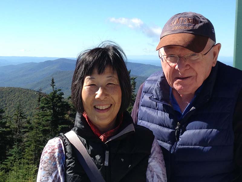 A couple stand together smiling in the mountains