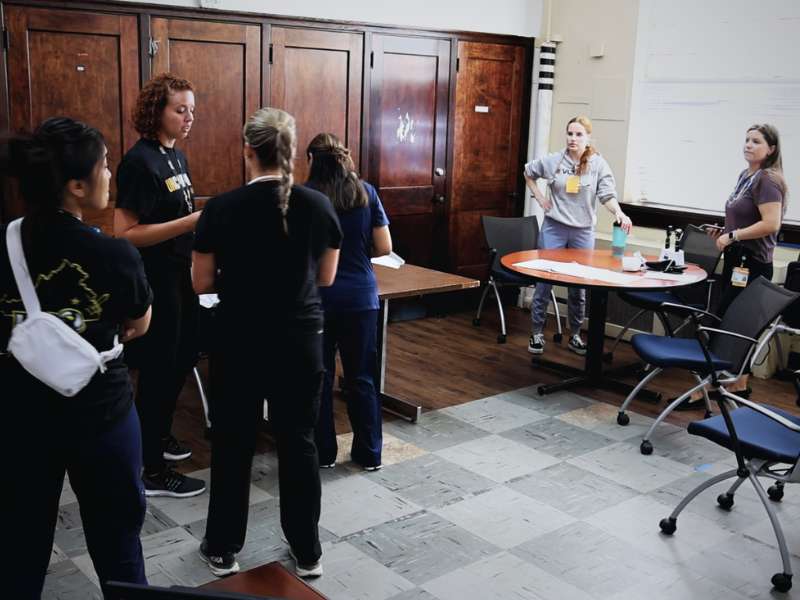 a team of family nurse practitioner students talks with their faculty lead while preparing to conduct back-to-school physicals