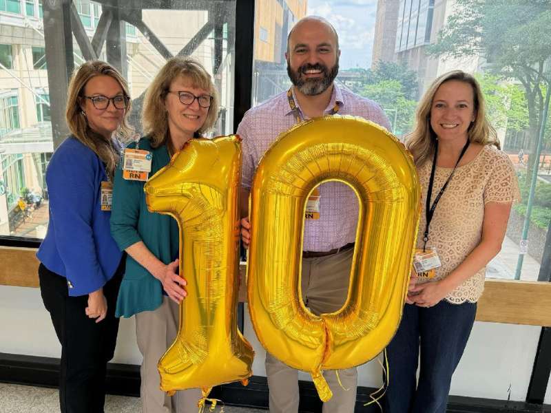 four people hold large gold balloons shaped as the number 10 in the VCU hospital in Richmond