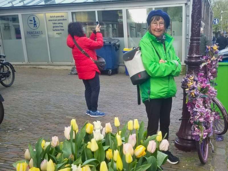 eileen tangley in a green raincoat and blue hat in front of a patch of yellow tulips