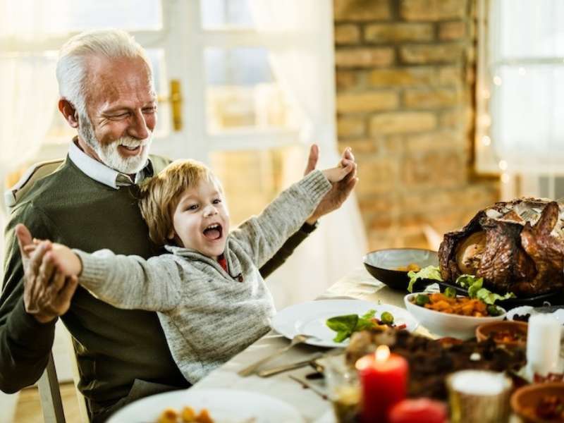 an older adult sits at a holiday dinner table with a toddler on their lap