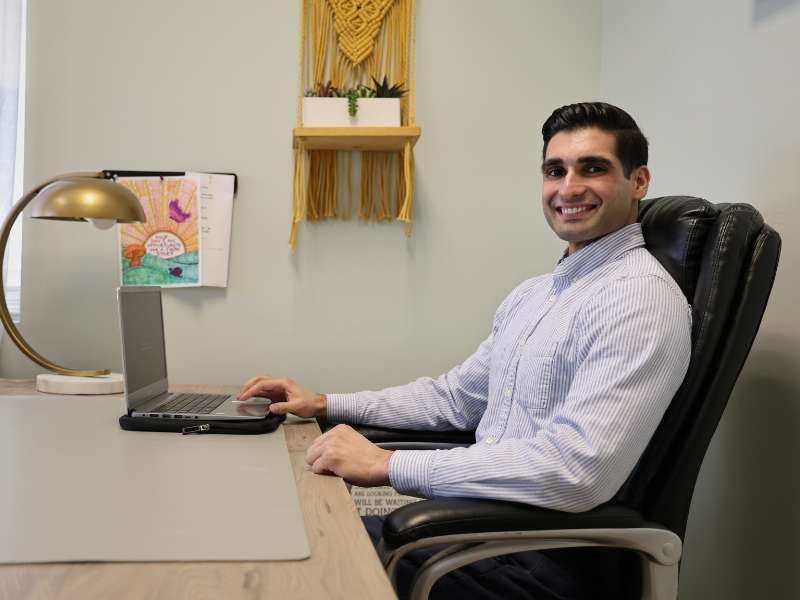 jag chahal sitting at a desk with one hand on his laptop while smiling