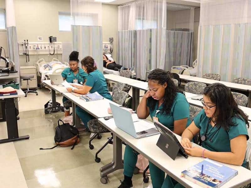 four nursing students seated at a table in a health clinic setting looking at laptop computers