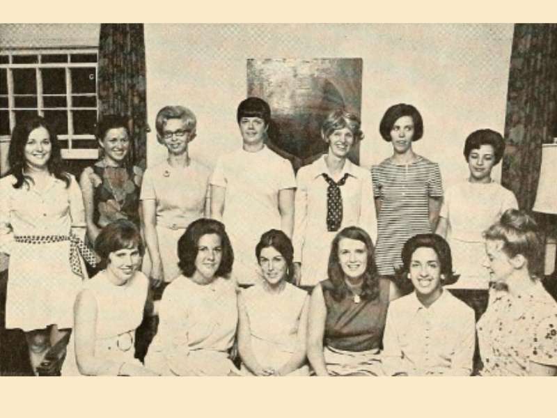 13 smiling young women posing in two rows in a black and white photo from the nineteen sixties