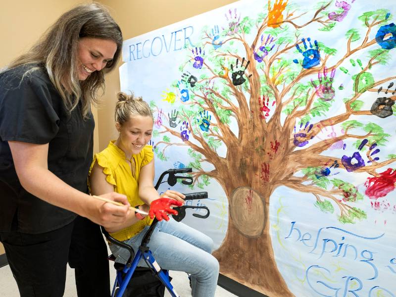 clinical research nurse laura stevens helps participant rylee joyce add her painted handprint to the study's mural