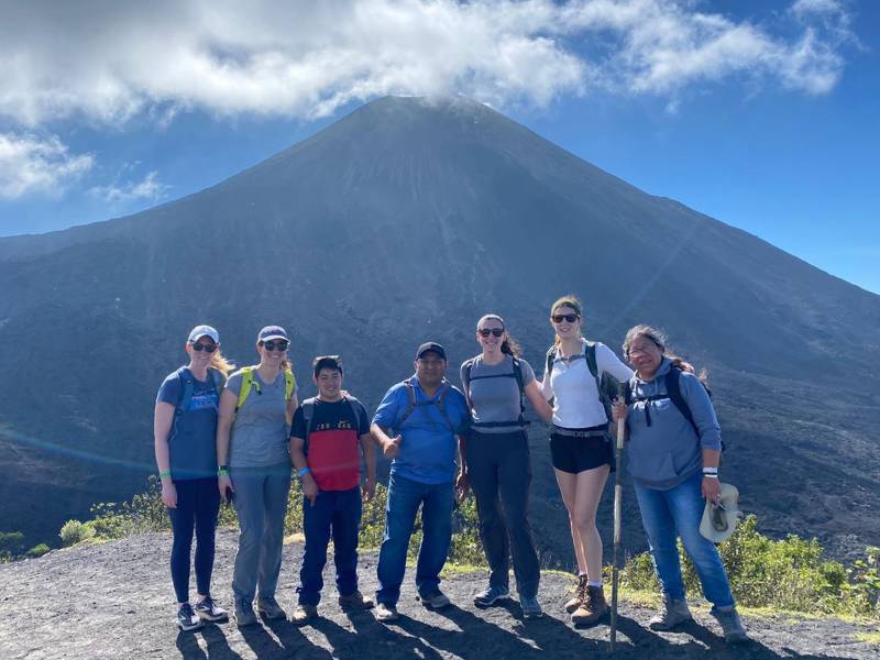 four v.c.u. students and three guatemalans dressed in hiking gear pose in front of a tall mountain