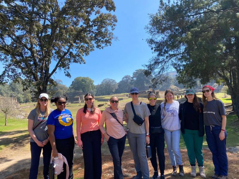 seven v.c.u. nursing students and two v.c.u. professors pose in front of ancient mayan ruins in a verdant setting