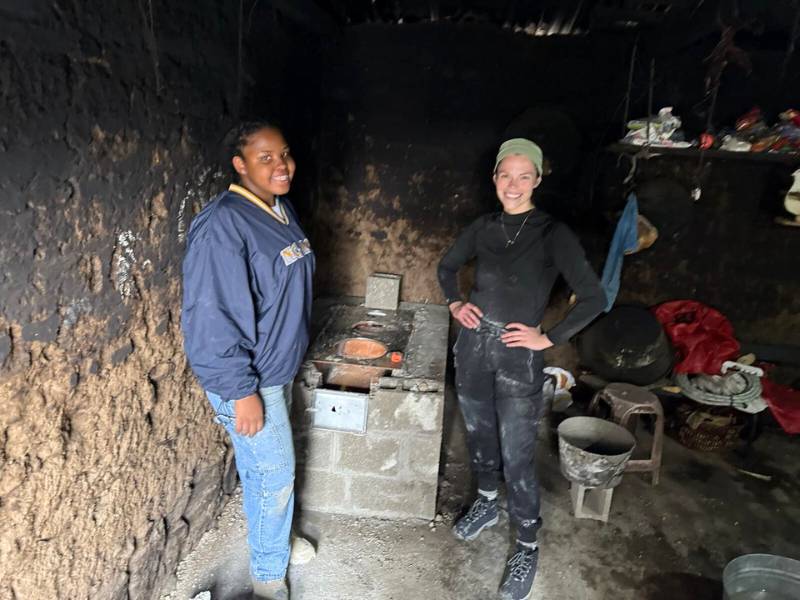 two v.c.u. students in dirty clothes in a dark room with concrete walls standing in front of a makeshift stove made of concrete