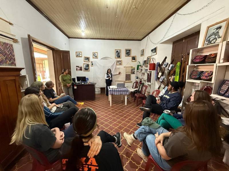 a group of seven v.c.u. nursing students and their two professors listen to a presenter leading a discussion in a room adorned with photos, fabrics, and colorful satchels