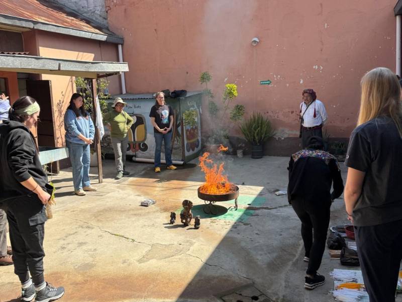 A group of seven people gathered around and staring at a small fire pit outside of a house