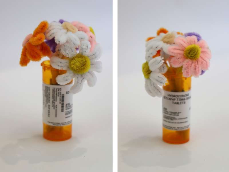 Two photos of an orange prescription pill bottle labeled 'Hydrocodone' being used as a vase for a bouquet of handmade flowers crafted from colorful pipe cleaners. The juxtaposition of medication and cheerful faux flowers suggests a commentary on healing, pain, or the intersection of medical and emotional well-being.