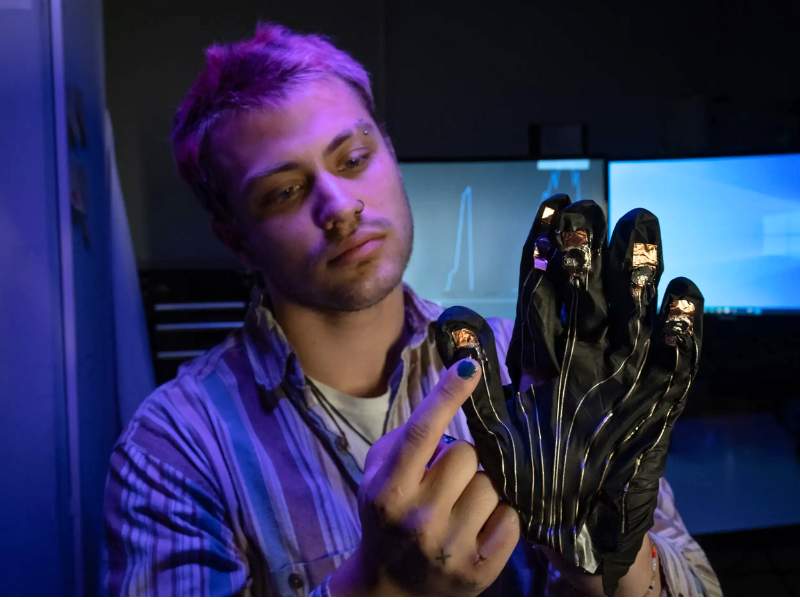 Phillip Glass, a physics graduate student, shows off pressure sensors on a glove, part of a suite of wearable prototypes to help patients with Parkinson’s disease.