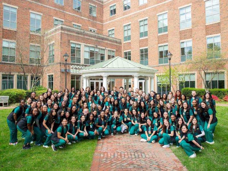 a group of v.c.u. nursing students in matching green scrubs and black vests pose together in the school garden