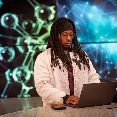 a student working on a laptop in front of a brightly colored wall featuring large displays of science images such as d.n.a. strands and molecules