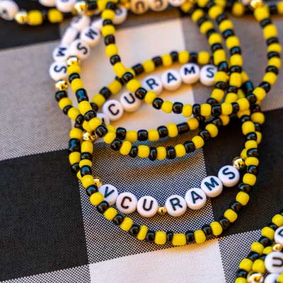 a pile of black and gold beaded bracelets with beads that spell out v.c.u. rams