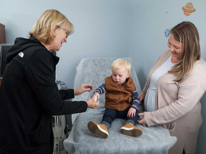 A nurse checks a toddler's blood pressure while the child's caregiver stands nearby, smiling.