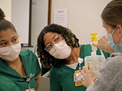 two nursing students look on while a preceptor demonstrates a task