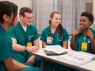 four nursing students at a table with notes scattered on it work together