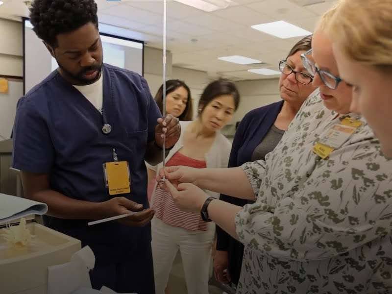 A nursing instructor demonstrates medical equipment to students gathered around during a classroom training session