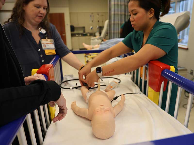 A nursing student practices a procedure on an infant simulation mannequin under instructor supervision