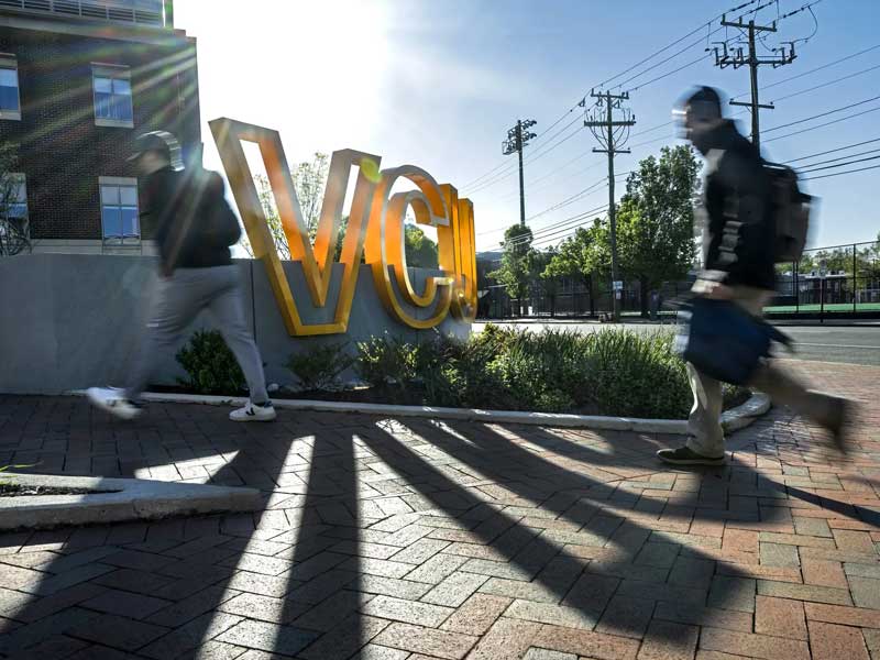 Students walk past a large yellow V.C.U. sign on Monroe Park Campus