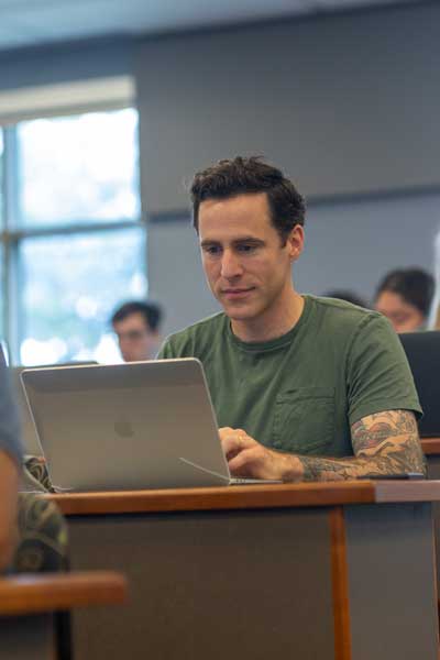 a student seated in a lecture hall taking notes on a laptop computers